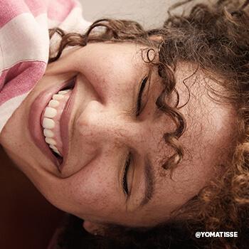 An image of a model with curly hair smiling big Mobile