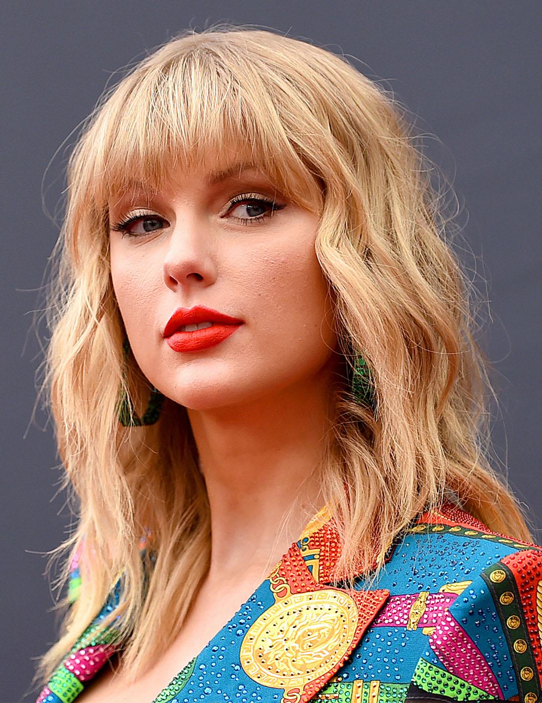 A photo of Taylor Swift flaunting her blonde shaggy hair paired with green hoop earrings and colorful top on a dark gray background Desktop