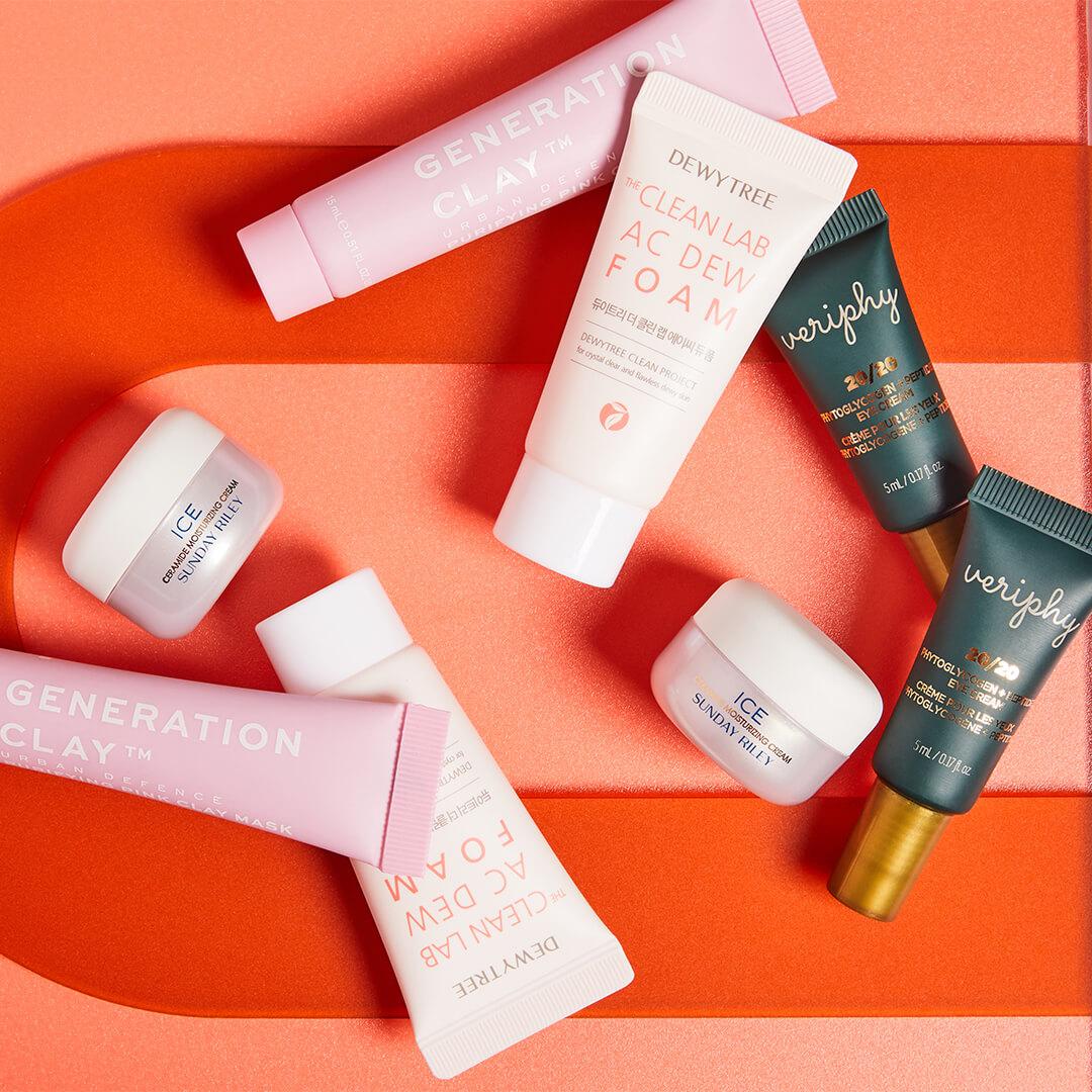 Skincare products from various brands on colorful red and orange background Desktop