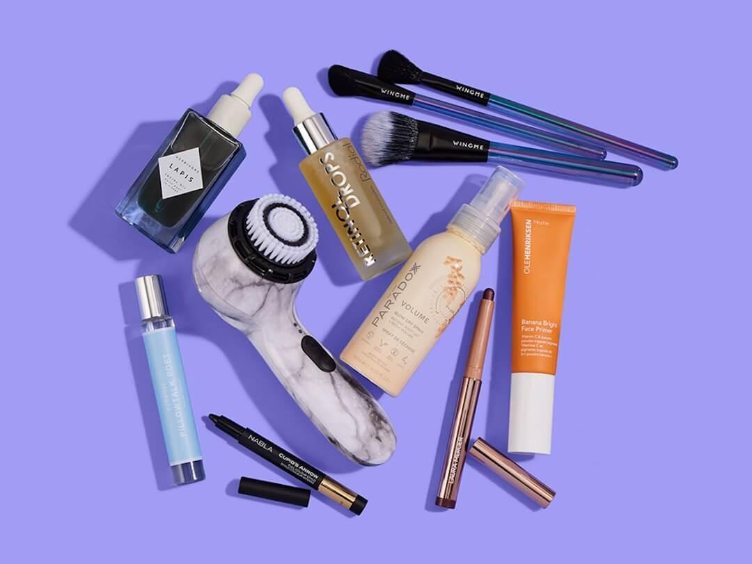 Skincare, makeup, and hair care products and tools from various brands scattered on purple background Desktop