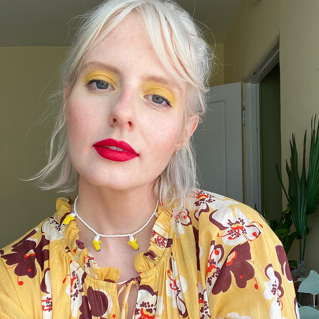 Close-up image of Hannah Cassidy rocking a bold yellow eyeshadow and bold red lipstick look in a yellow floral outfit Mobile