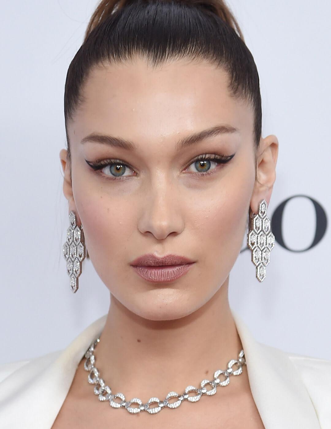 Bella Hadid looking fierce in a white dress, silver necklace and earrings, and a negative space eyeliner makeup look Desktop