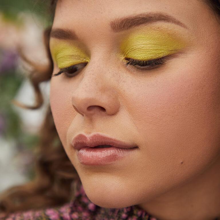 A close-up image of a model wearing neon lime green eyeshadow looking down Desktop