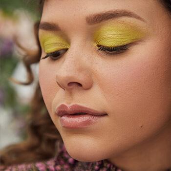 A close-up image of a model wearing neon lime green eyeshadow looking down Mobile
