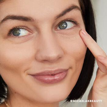 A closeup image of a model with short black hair touching the skin under her eye with one finger Mobile