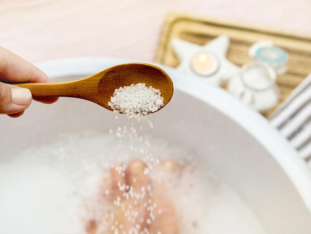 Image of hand holding a wooden spoon with magnesium chloride vitamin salt and foot bath as background Desktop