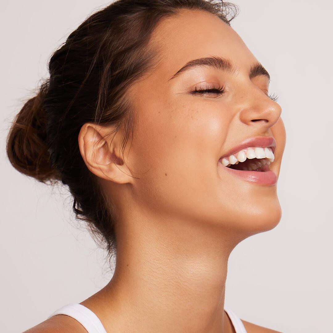 Side profile close-up of a model with clear skin smiling big while eyes closed Mobile