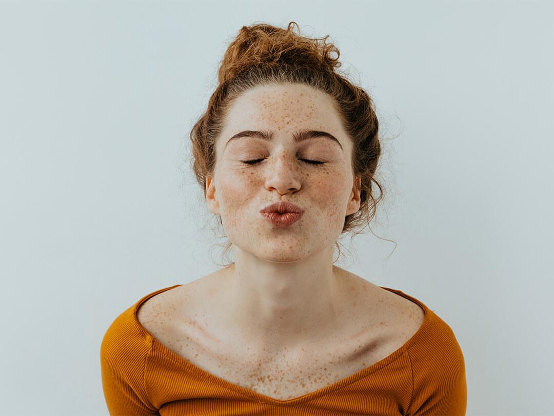 Close-up of a girl in a dark orange shirt pouting her lips with eyes closed Desktop