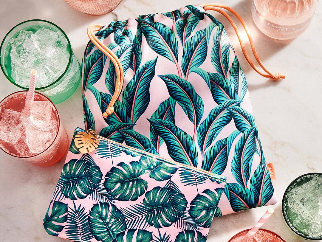 August 2022 IPSY Glam Bag and Glam Bag Plus bags on white marble with glasses of pink and green drinks Desktop