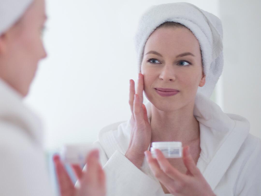 Mature woman in bathrobe putting on face cream in front of the mirror Desktop