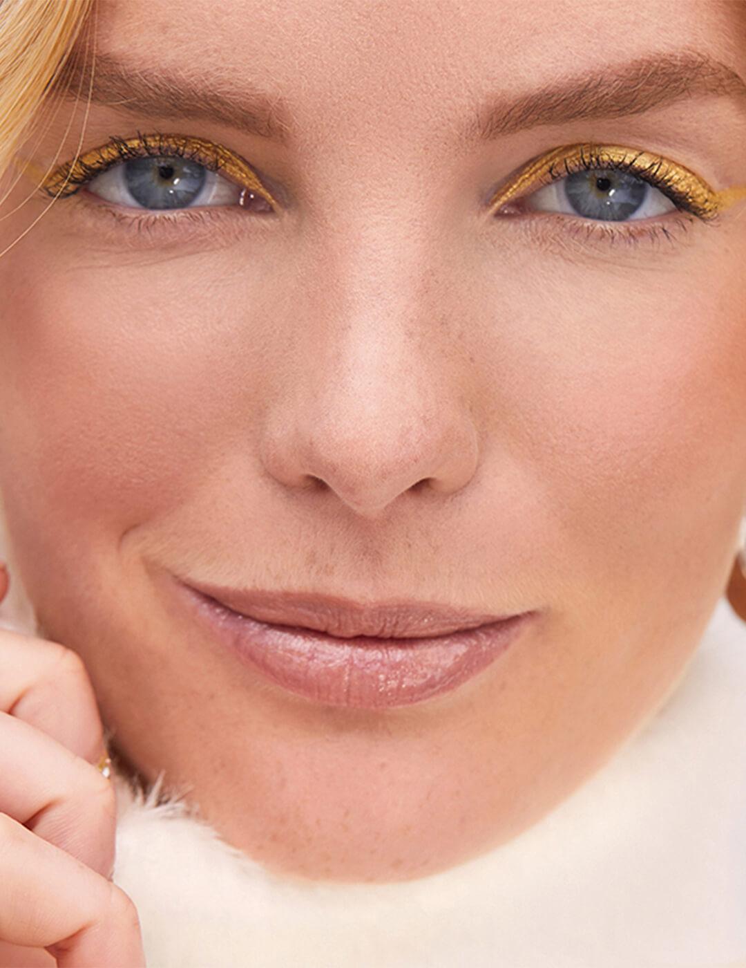Close-up of a smirking model rocking a gold eyeliner makeup look Mobile