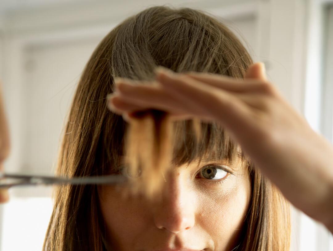 An image of a green-eyed brunette woman focused on trimming her hair on a white background Desktop