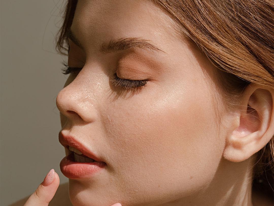 An image of a woman with her eyes closed, showcasing her nails and light, clean girl makeup Desktop