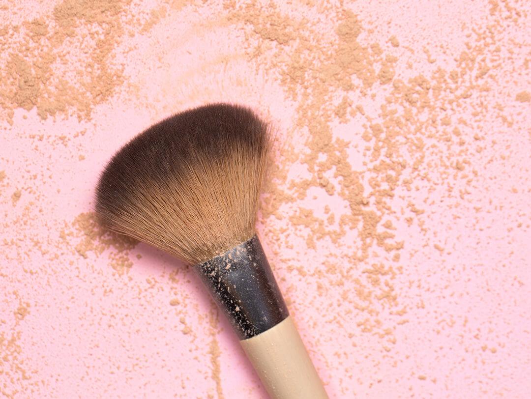 Top view of face makeup brush and face makeup powder on light pink background Desktop