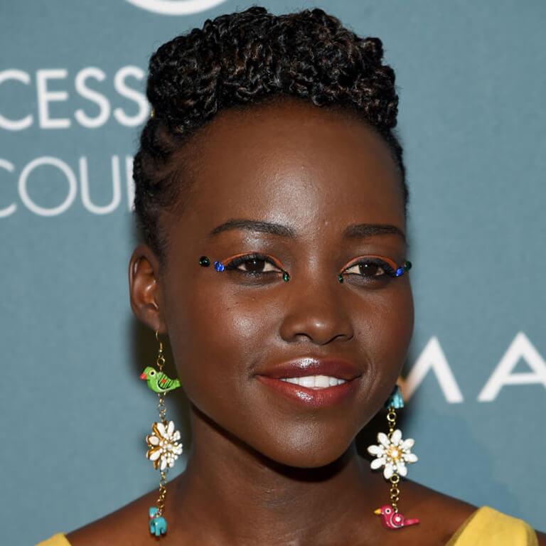A close-up image of Lupita Nyong'o rocking a bold eyeshadow look, twisted top and cornrows hairstyle, and statement dangling earrings Desktop