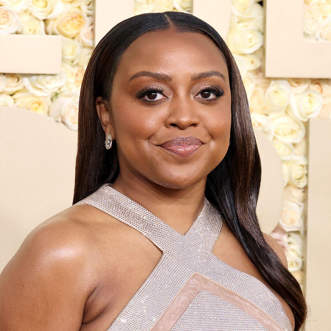 A picture of Quinta Brunson with her hair done in a sleek manner, wearing a mauve monochromatic makeup and a silver silk halter dress Mobile