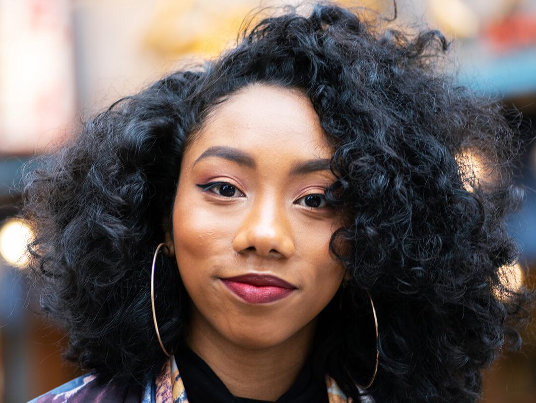 Image of a young, Black American woman with curly hair and big hoop earrings against busy street background Desktop
