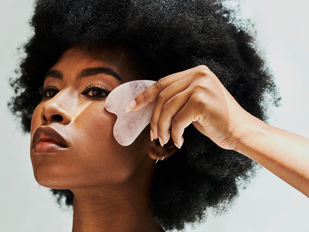 Beautiful young woman using gua sha quartz stone on her face for a skincare routine Desktop