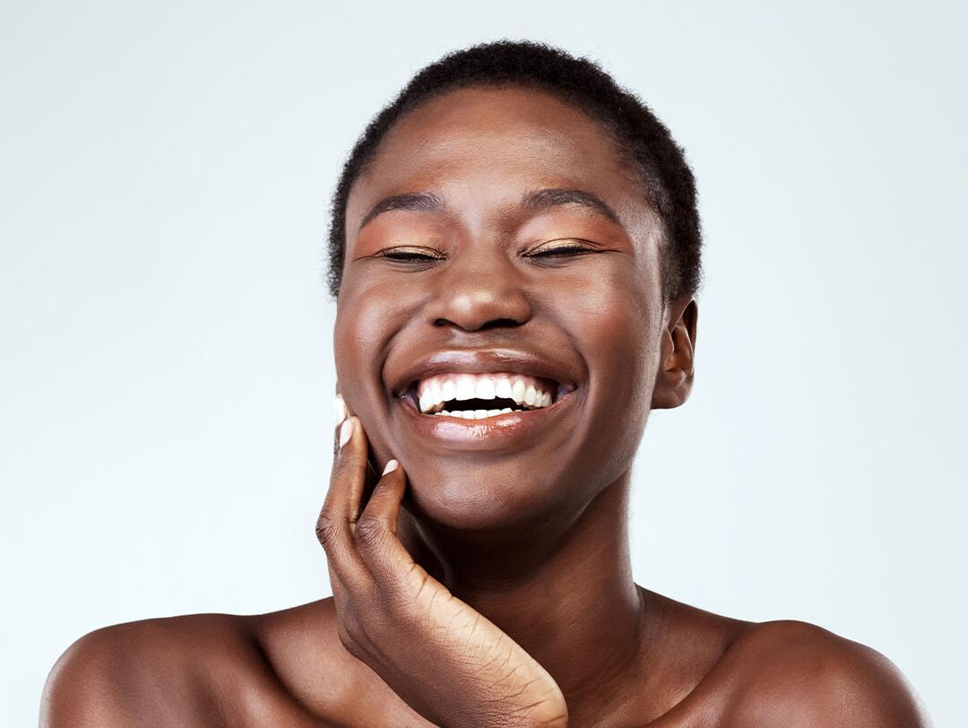 Young black woman smiling while holding her cheek against a grey background Desktop