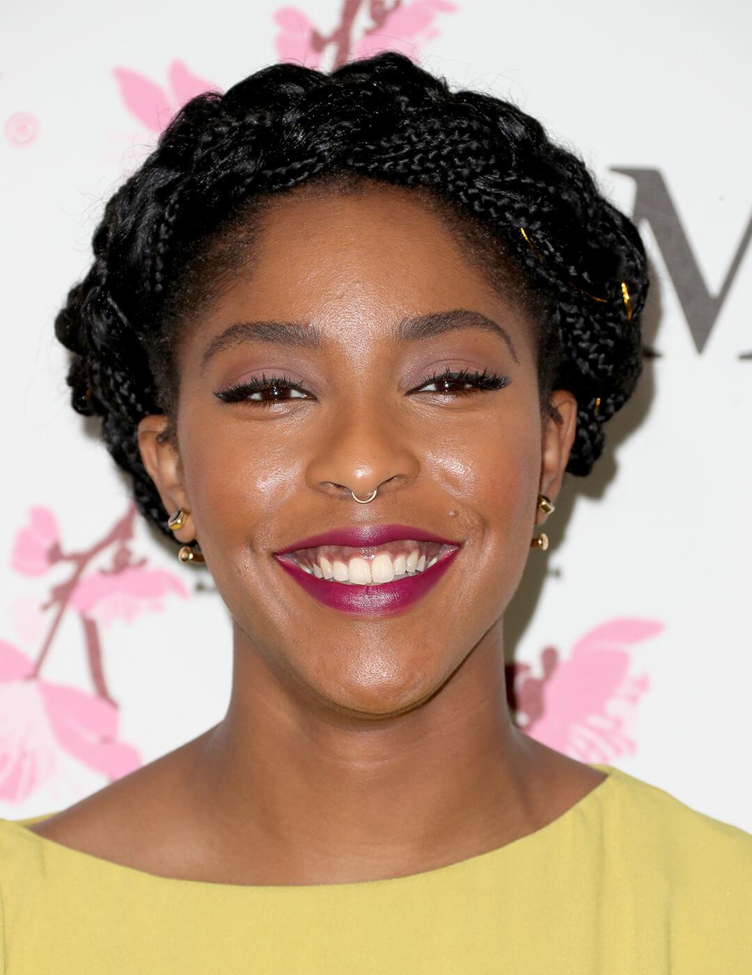 Smiling Jessica Williams rocking a yellow dress and halo braids hairstyle on the red carpet Mobile