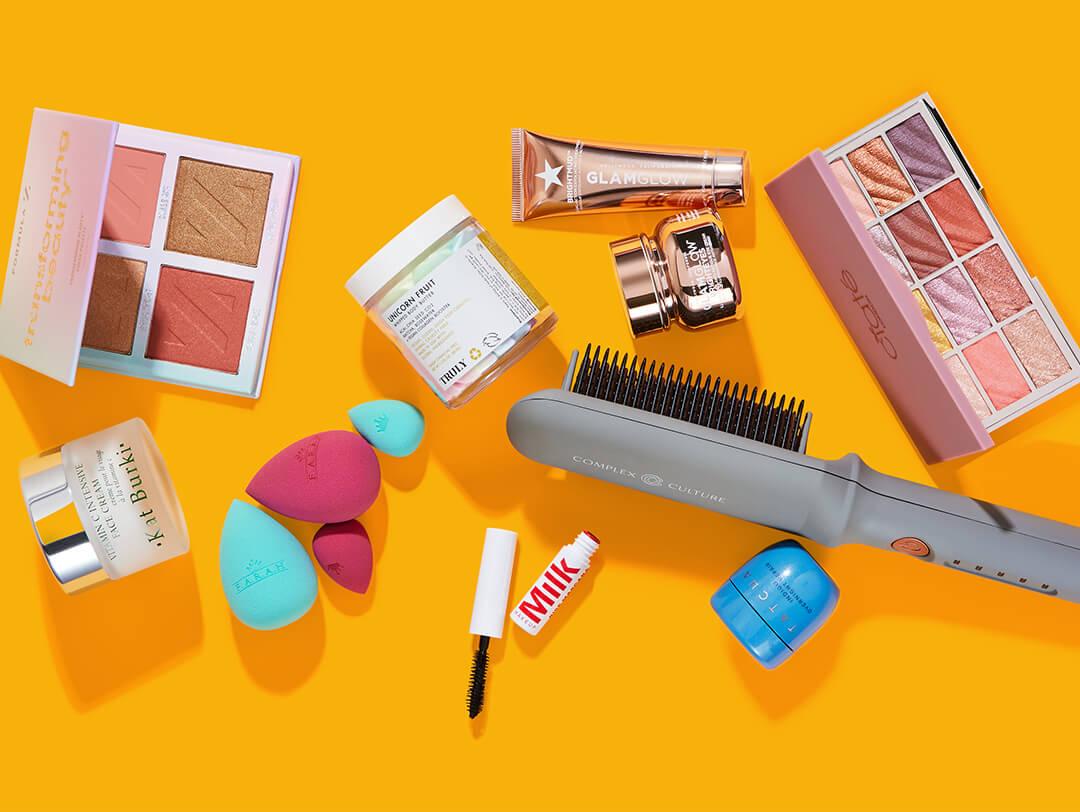 Beauty and makeup products from various brands scattered on bright orange background Desktop