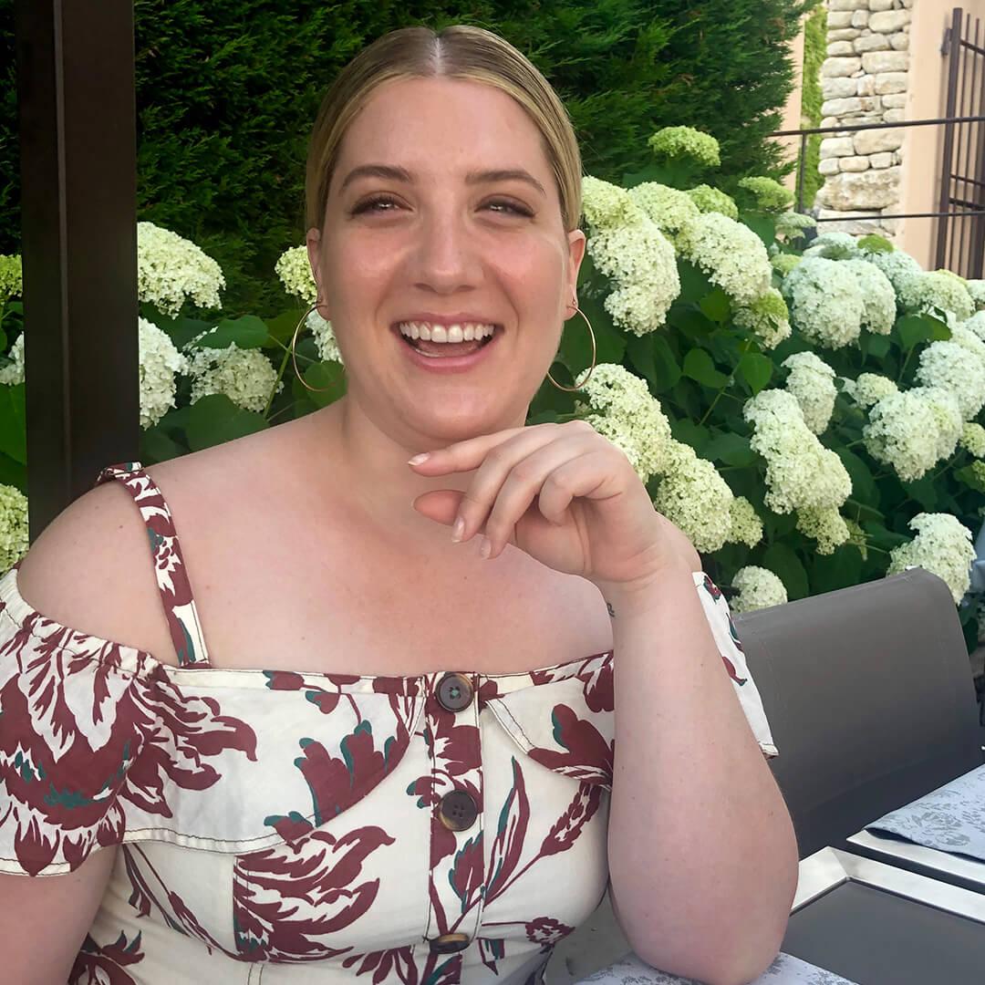 Close-up image of Maddie Aberman smiling while posing with white flowers in the background Desktop