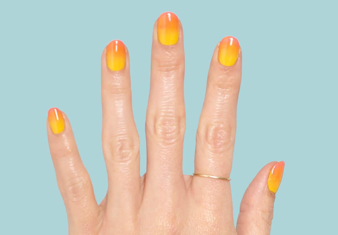 Close-up image of a hand with a yellow to orange ombré gradient nail art mani against a teal background Desktop