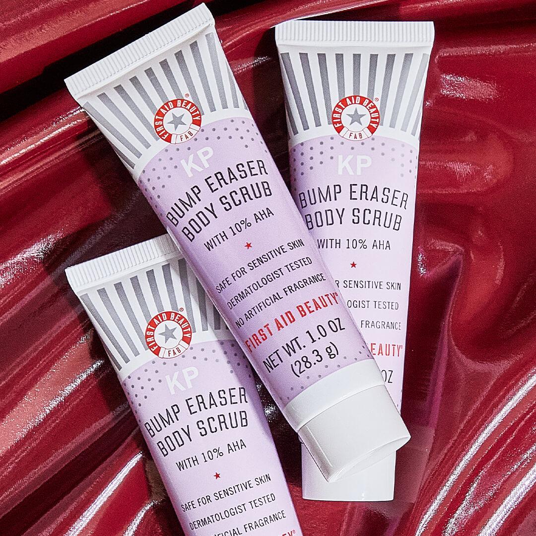 Three tubes of FIRST AID BEAUTY KP Bump Eraser Body Scrub with 10% AHA on glossy, dark red leather cloth Desktop