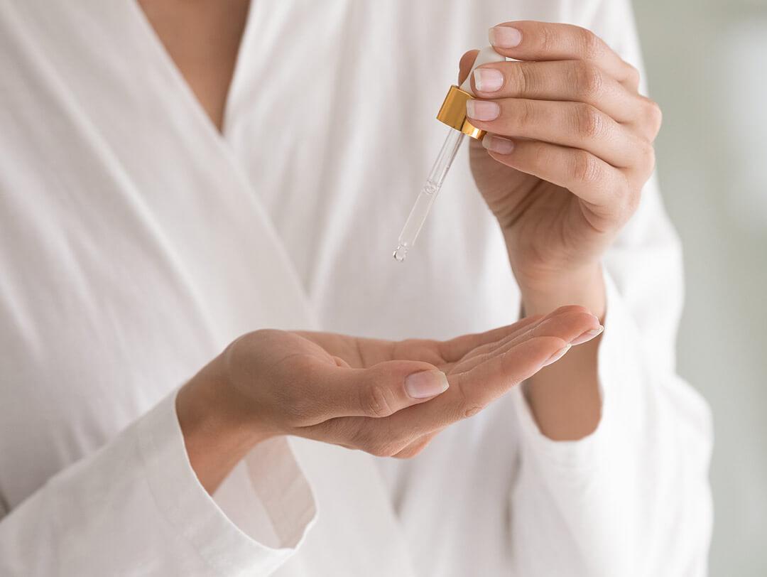 Close-up of a woman in a white robe's hands putting serum from a medicine dropper Desktop