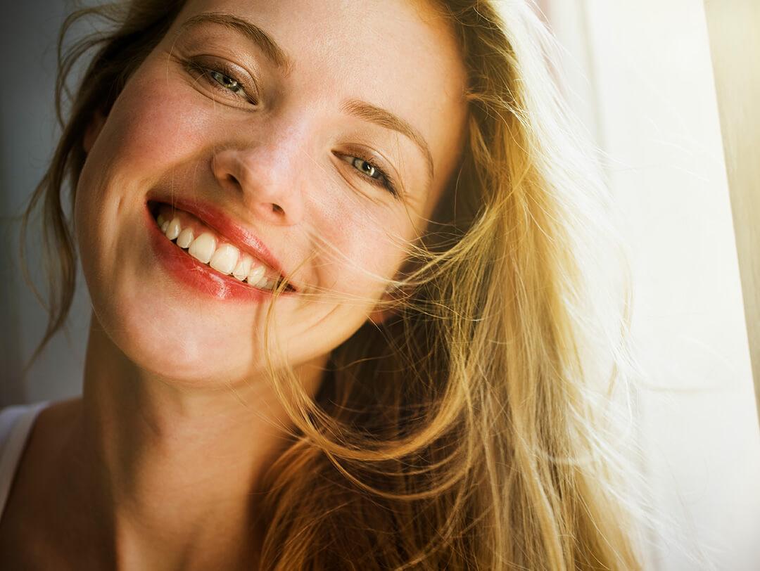 A photo of a woman smiling with glowy skin and a soft light background Desktop