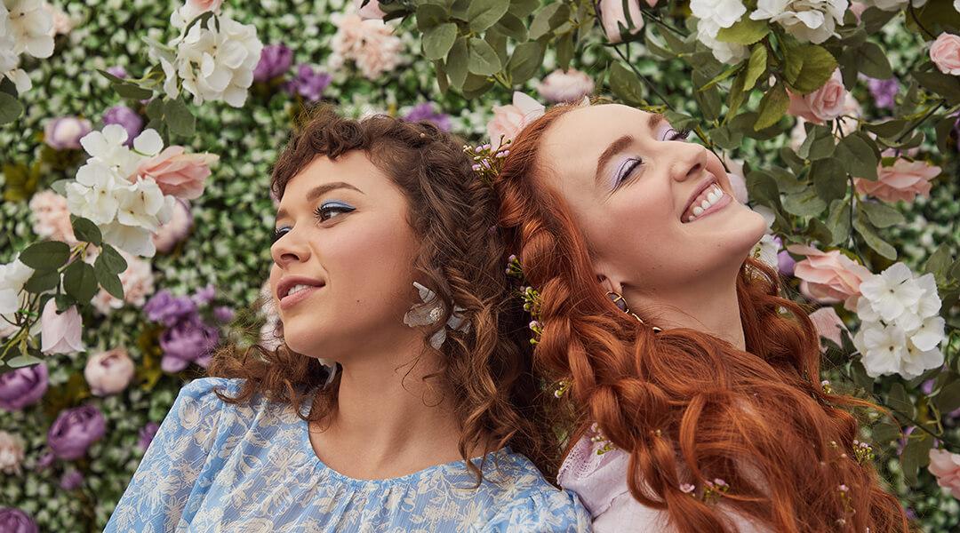 An image of two models standing back to back in front of a wall of flowers. Desktop