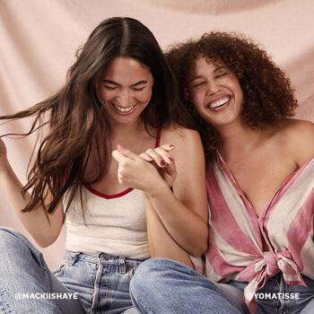 An image of models with wavy and curly hair holding hands while smiling big Mobile