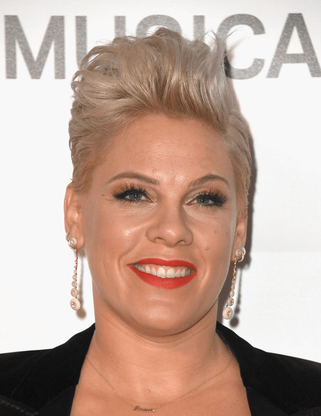 Pink rocking a black suit, gold dangling earrings, bold lip makeup look and faux hawk hairstyle Desktop