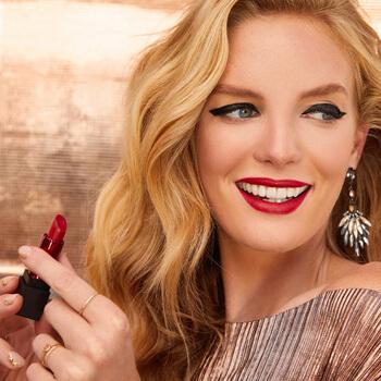 An image of a model wearing a bold cat eye look and red lipstick holding a lipstick with her fingers Mobile