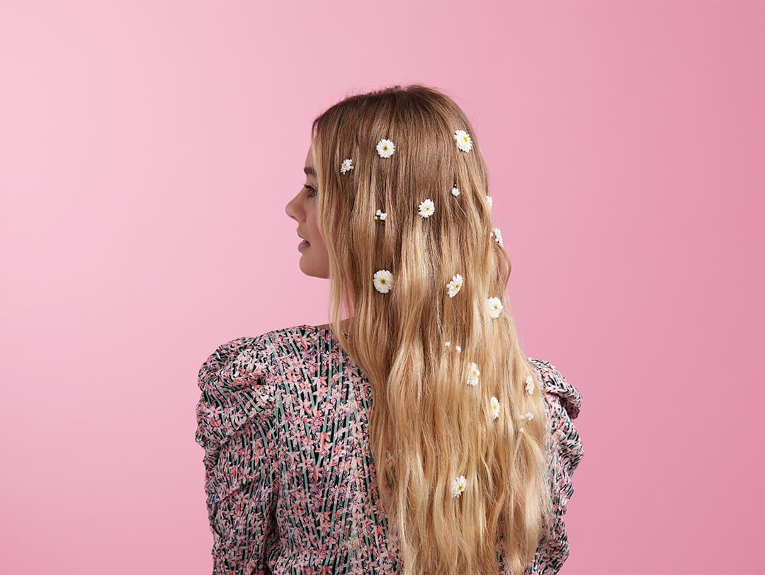 An image of model with long blond hair embellished with white flowers wearing a floral outfit Desktop