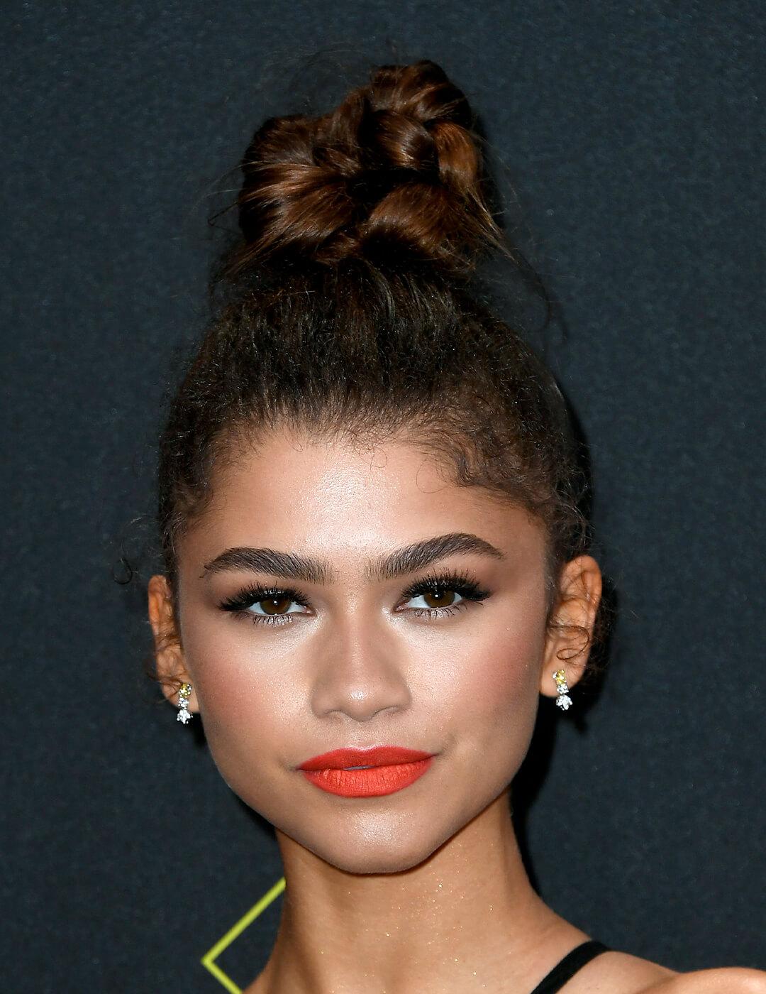 Zendaya looking glam in a top knot hairstyle paired with a bold coral lipstick Mobile
