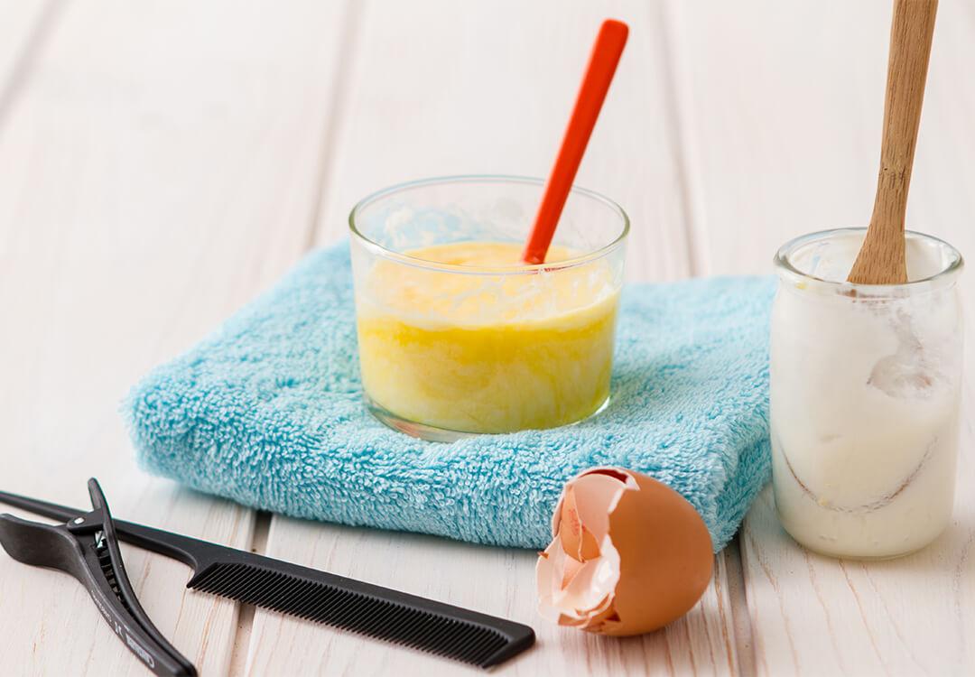 Image of glasses with yogurt and egg mask, egg shell, hair clip, and comb on wooden surface Desktop