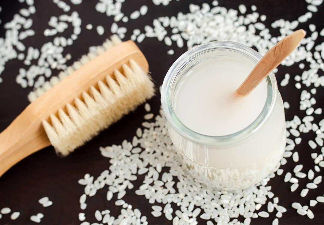 Jar of rice water with wooden spoon on black ground with rice scattered and wooden brush Desktop