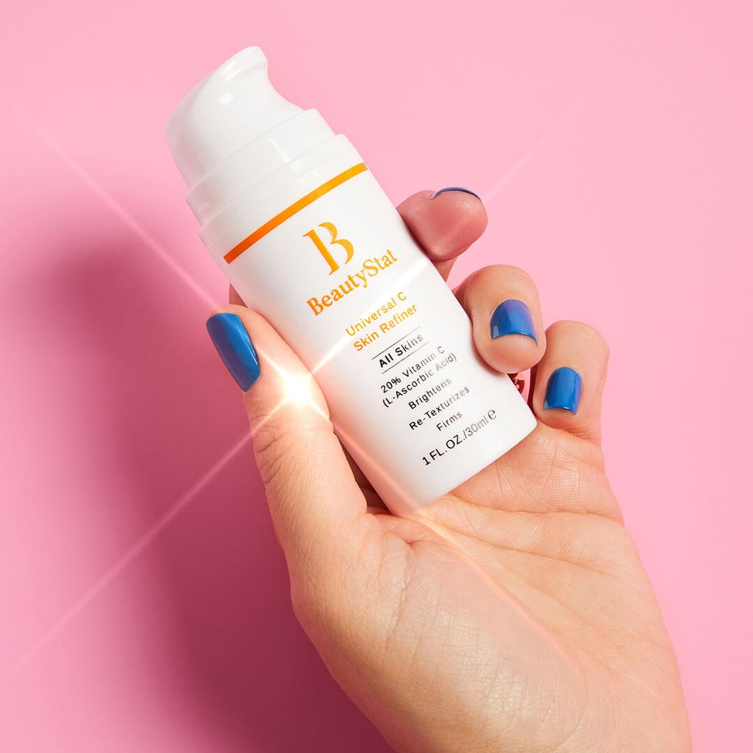 Image of a hand with blue nail mani holding the BEAUTYSTAT Universal C Skin Refiner with lens flare on pink background Mobile