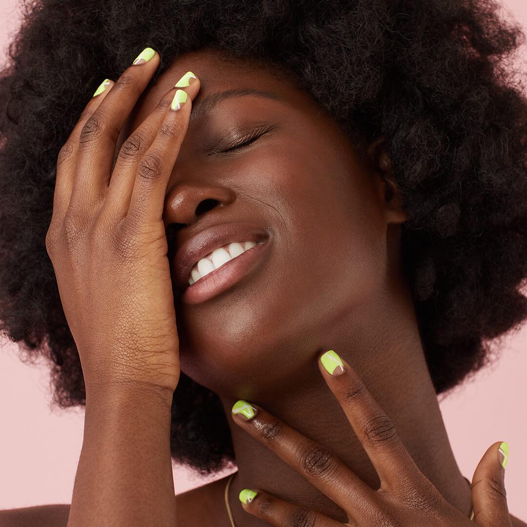 Close-up of a black model with slime green nail art posing with eyes closed against pink background Desktop