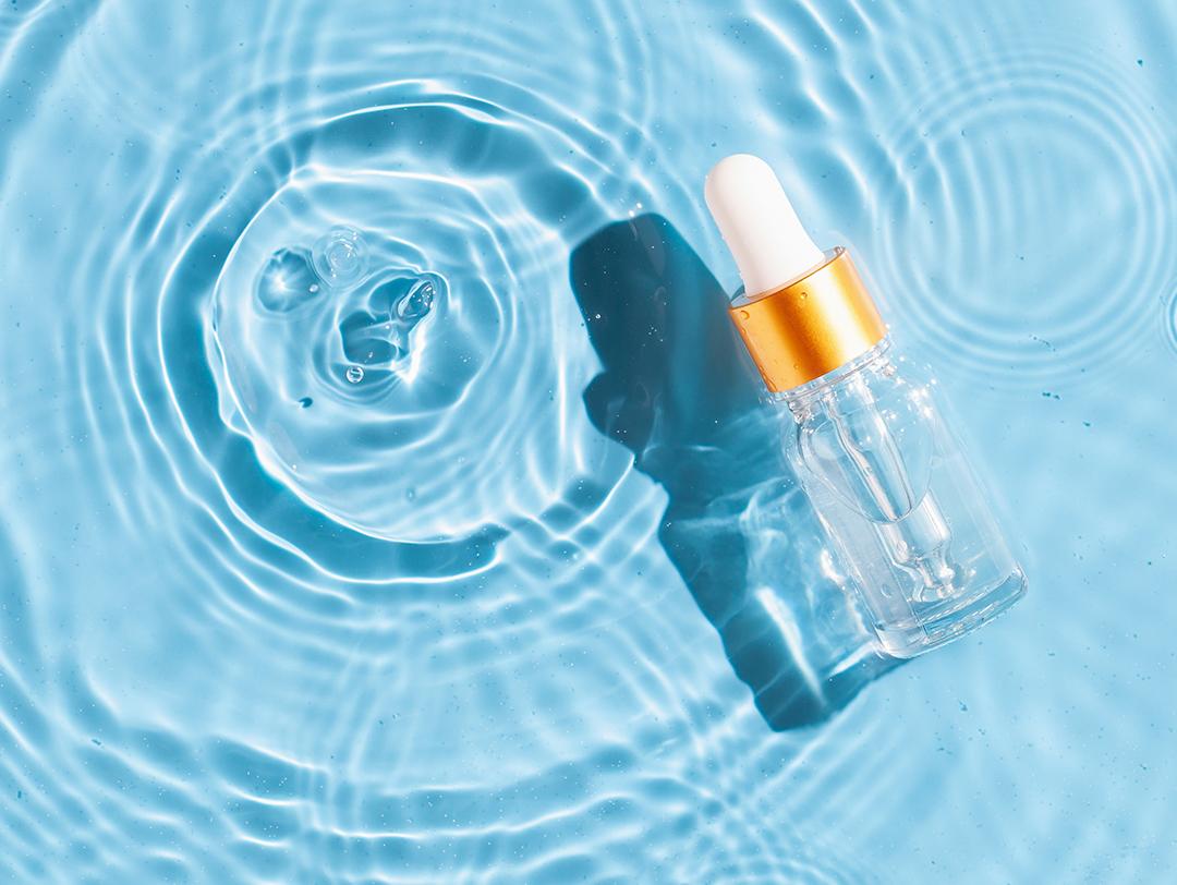 A photo of a serum bottle floating on water with splash effects and a blue background Desktop