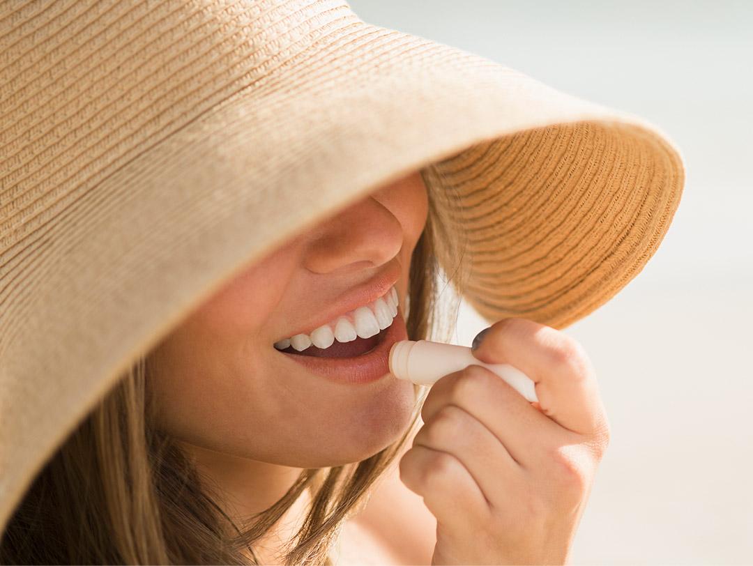 A photo of a woman with a sun hat applying lip balm Desktop