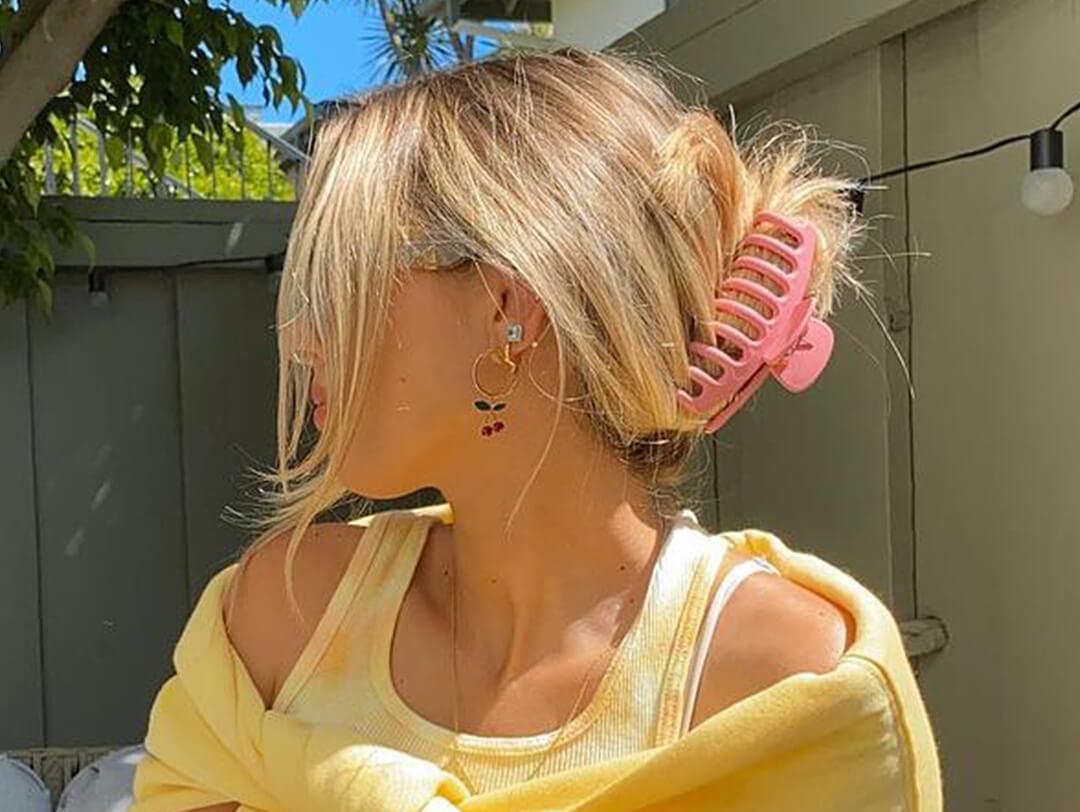 Close-up of a woman with pink clamp on her hair and yellow outfit posing in her backyard Desktop