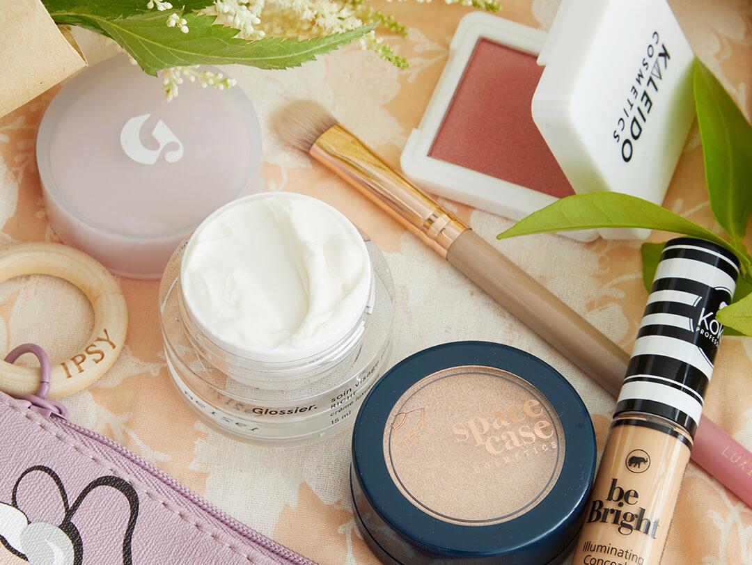 Flat-lay image of IPSY April 2020 Glam Bag, skincare, and makeup products and tools on top of floral patterned textile Desktop