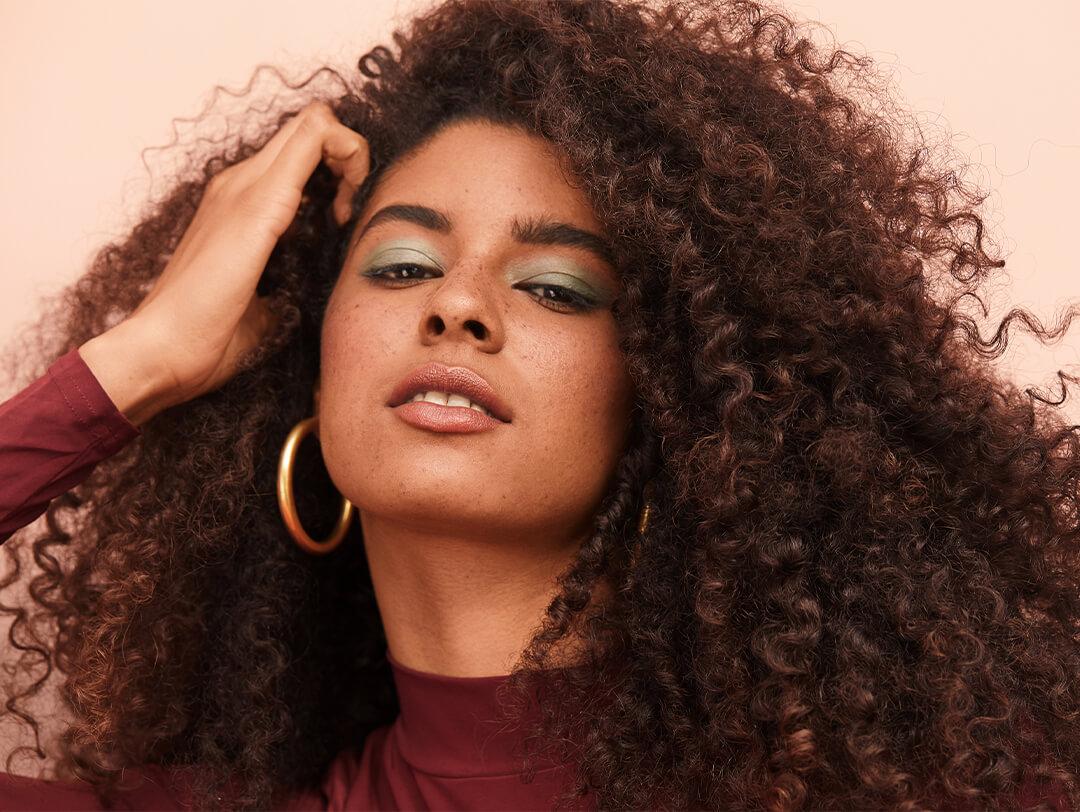 Close-up image of a model with curly hair wearing big hoop earrings and green eyeshadow posing Desktop