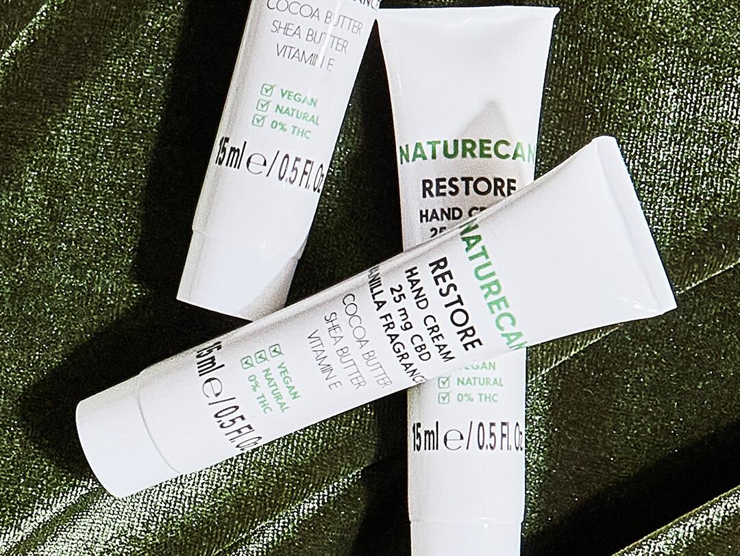 Three tubes of NATURECAN Restore CBD Hand Cream on dark green velvet cloth Desktop