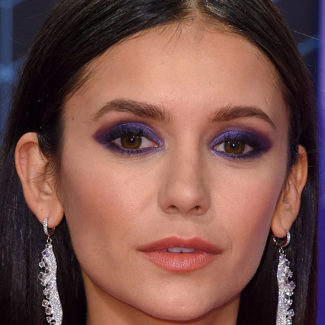 Close-up image of Nina Dobrev rocking a dark purple eye makeup look and silver feather earrings Desktop
