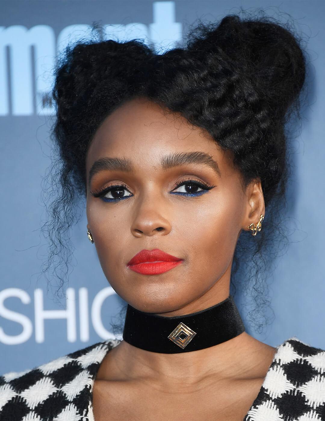 A photo of Janelle Monae styled her black curly hair into space buns wearing a black choker, a shade of red lipstick and a blue eyeliner Desktop