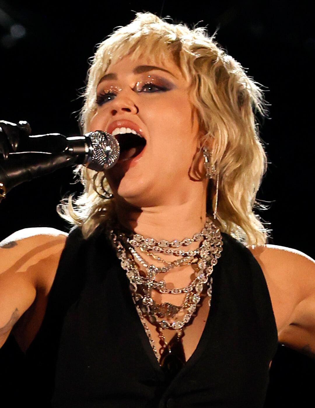 Miley Cyrus with a blonde mullet, glittery eyeshadow makeup look singing Mobile
