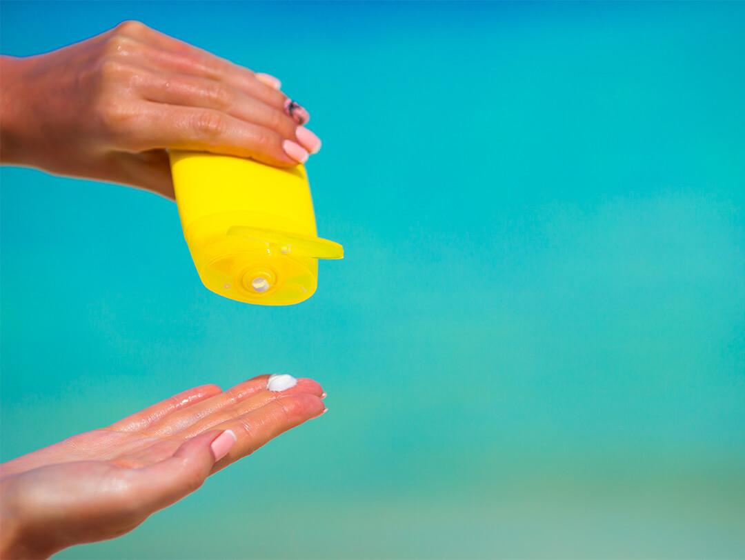Image of a woman's hands with yellow suncream bottle and the blue sea as background Desktop
